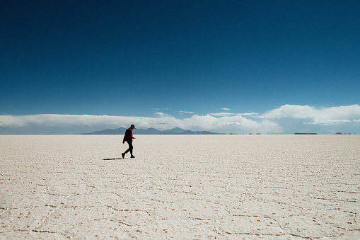 Alone hipster traveler walking in wide salt flat in Salar de Uyuni, Bolivia in a middle of the sunny day at dry season