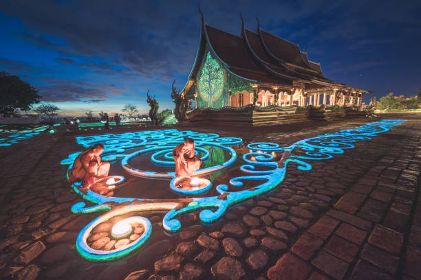 Ubon Ratchathani , Thailand - November 23, 2015 ; Group of monk light candle and praying in Sirindhorn Wararam Phu Prao is public Temple (Wat Phu Prao) at evening a glow of the sculpture of the Kalpapruek, which is attached to the wall behind the church.It will appear green glow in the night