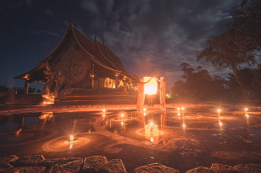 Ubon Ratchathani , Thailand - November 25, 2015 ; Group of monk light candle and praying in Sirindhorn Wararam Phu Prao is public Temple (Wat Phu Prao) at evening a glow of the sculpture of the Kalpapruek, which is attached to the wall behind the church.It will appear green glow in the night