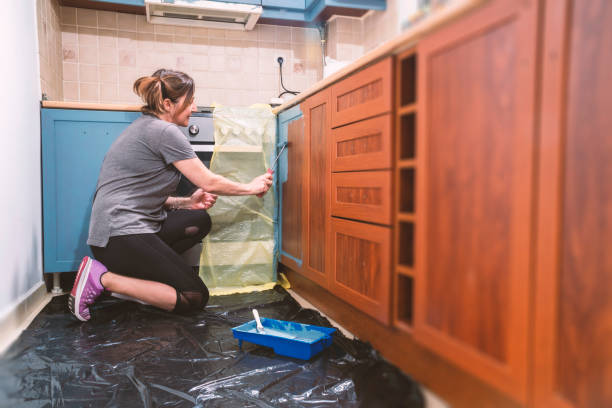 Painting kitchen. Mid age woman painting her old brown kitchen to blue modern color. Improving home is the main hobby for lockdown days. kitchen cabinet refacing stock pictures, royalty-free photos & images