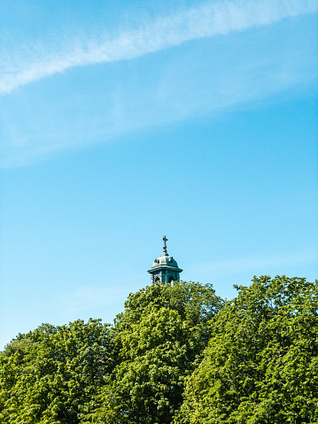 The peak of a church tower and cross is visible from behind the trees on a summer day in Sweden.