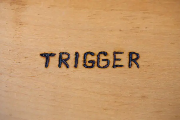 Photo of the word trigger handwritten on flat bare plywood surface with woodburner