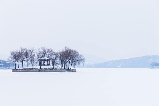 The snow covered park is full of white. The lake is frozen, and the Chinese Pavilion surrounded by trees in the center of the lake is very beautiful.