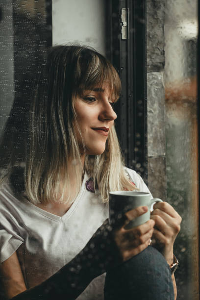istock Raindrops, Woman Looking Out The Window and Drinking Coffee 1249390204