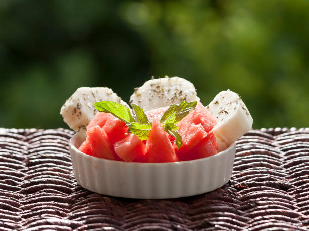 Small bowl with watermelon, three slices of Cypriot halloumi cheese and fresh mint leaves on garden table in sunlight