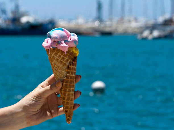 istock Ice cream cone in hand in front of blue sea 1249392866