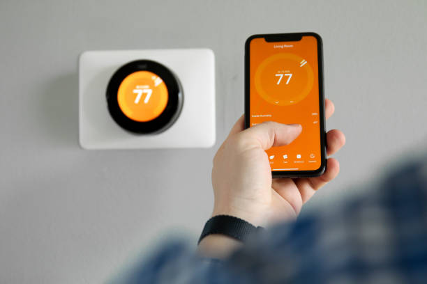 el hombre utiliza un teléfono móvil con aplicación de casa inteligente en la sala de estar moderna - termostato fotografías e imágenes de stock