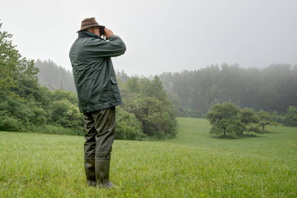 istock Hunter in the rain, watch a small idyllic valley through his binoculars. 1249400560
