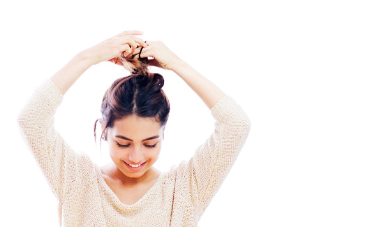Portrait of a young woman making a messy bun with her hair and smiling - isolated over white