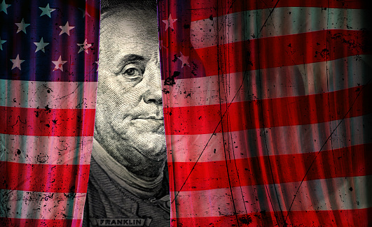 Conceptual finance and economy image of American one hundred dollar bill and damaged American flag stage curtain.
