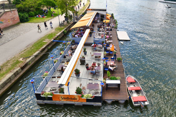 Frankfurt am Main, Germany - June 2020: View from bridge on restaurant with tourists on a boat called 'Bootshaus' on Main river in Frankfurt