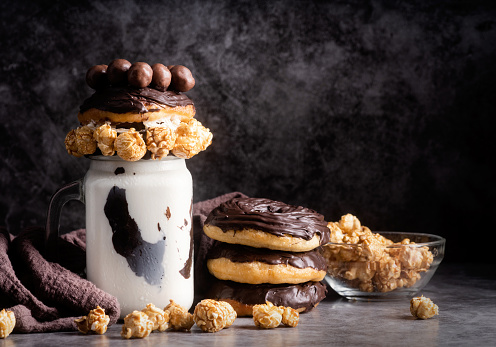 Ice cold chocolate donut milkshake in a mason jar decorated with caramel popcorn, whipped cream and cocoa candies, low key