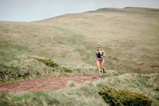 Action photo of athlete woman trail runner running and climbing on mountain.