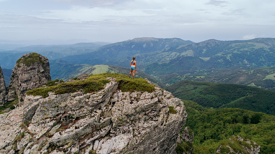 Young woman relaxing and enjoying the view during hard trail running training on the top of mountain. She wears sport clothing and standing on top of mountain.