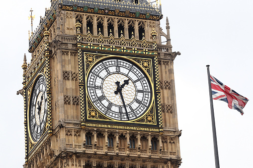 A close up view of the clock face of Big Ben and the Elizabeth Tower with the Union Jack flying in the City of Westminster - London, England
