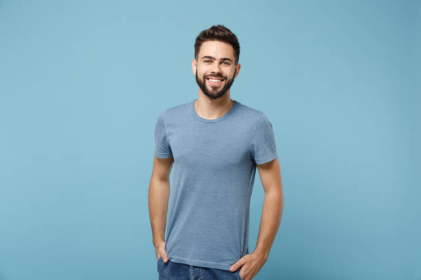 young smiling handsome man in casual clothes posing isolated on blue wall background, studio portrait. people sincere emotions lifestyle concept. mock up copy space. holding hands in pockets. - homem imagens e fotografias de stock