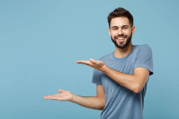 istock Young attractive handsome smiling man in casual clothes posing isolated on blue wall background, studio portrait. People sincere emotions lifestyle concept. Mock up copy space. Pointing hands aside. 1249420385