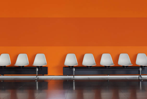 White chairs in a row against an orange wall inside a modern building. Empty chairs in a waiting room