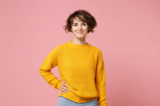 jeune fille de femme de brunette de sourire dans le chandail jaune posant isolé sur le fond rose pastel de mur, verticale de studio. les gens sincères émotions concept de style de vie. mock up espace de copie. je regarde la caméra. - mannequin métier photos et images de collection