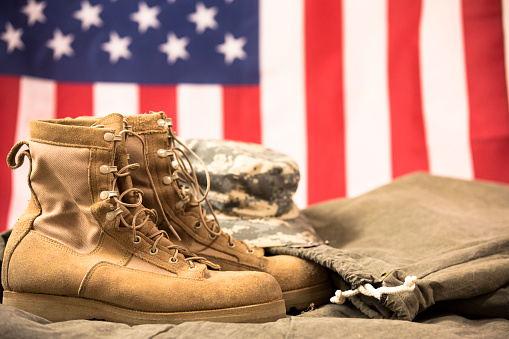 USA military boots, hat and dog tags with American flag in background.  No people in this US Memorial Day or Veteran's Day image.