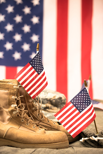 USA military boots, hat and dog tags with American flag in background.  No people in this US Memorial Day or Veteran's Day image.