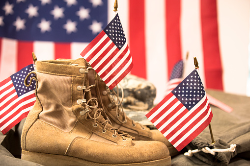 USA military boots, hat and dog tags with American flag in background.  No people in this US Memorial Day or Veteran's Day image.