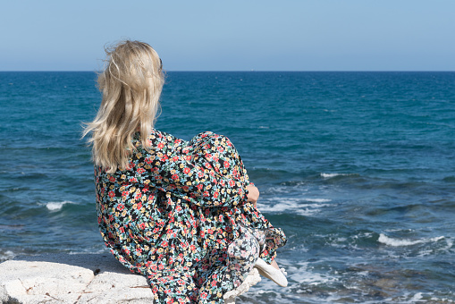 Woman in dress sitting on the rock beside the sea