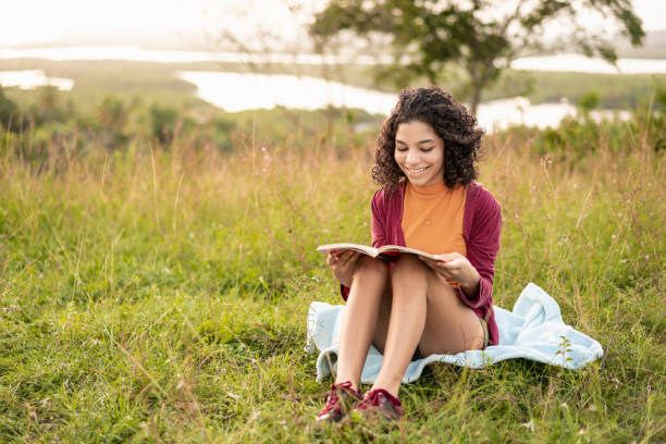 adolescente leyendo un libro y disfrutando de la puesta de sol - childrens literature fotografías e imágenes de stock