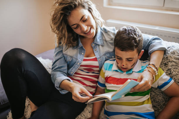 istock Young woman reading book to her son on sofa 1249445444