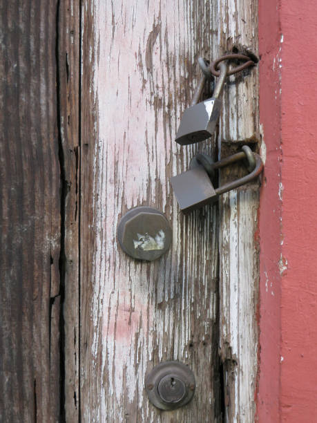 istock Padlocks and rusty iron chain on broken white old wooden door with violet graffiti. Locks on a chain hangs on a door. Old metal padlocks on a uncorked wooden door. 1249446868