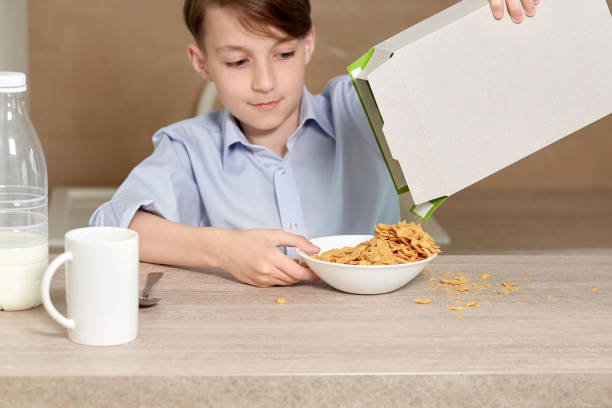 istock Beautiful baby boy pours cornflakes from a paper box into a white plate. 1249447596