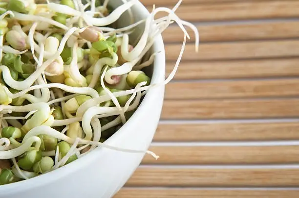 Close up of mung beansprouts in a white china bowl on a bamboo placemat.  Cropped in-camera on left side.