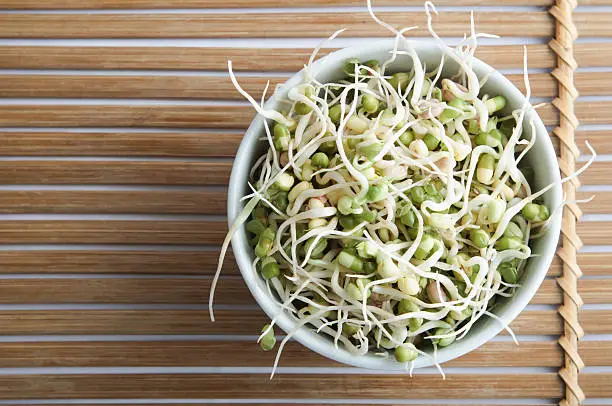 Overhead shot of a bowl of mung beansprouts, standing on a slatted bamboo mat.