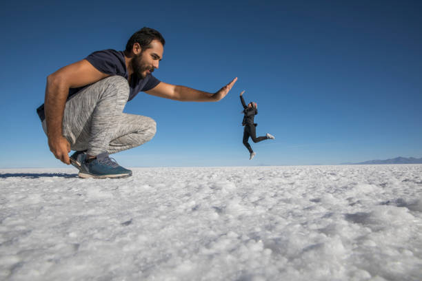 Couple playing with perspective in desert salt flats Couple playing in the desert salt flats, having fun with perspective illusion photos stock pictures, royalty-free photos & images
