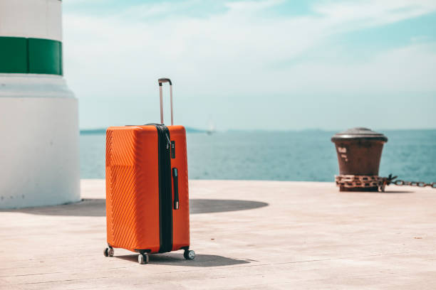Orange passenger suitcase next to the lighthouse waiting for the ship