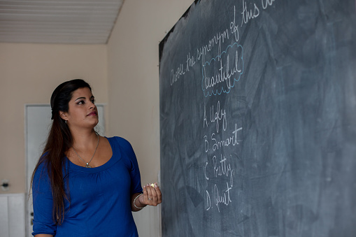 Female teacher at a rural school writing a question on a blackboard with a chalk - Developing countries concepts