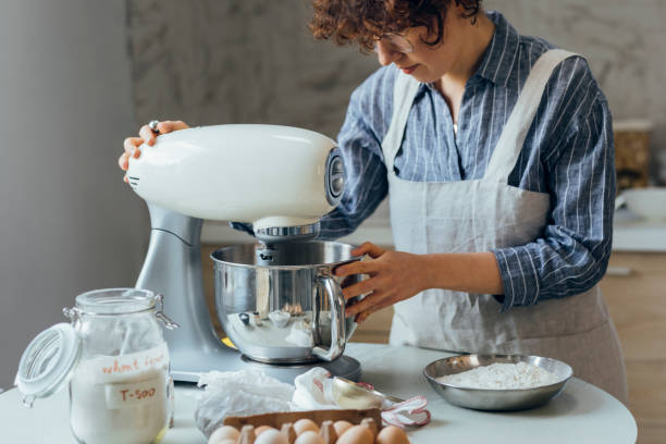 Happy Woman Using a Stand Mixer to Make Cookie Dough Woman in an apron mixing cookie dough in the kitchen. electric mixer photos stock pictures, royalty-free photos & images