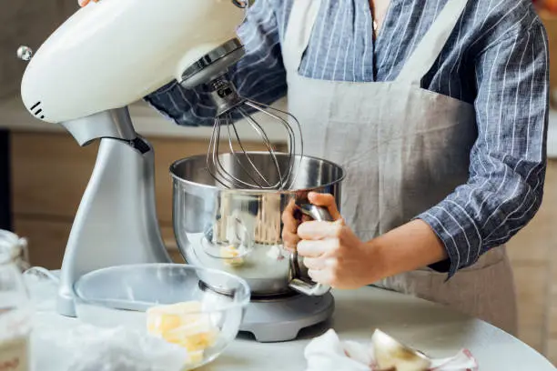 Hands of a woman in an apron using a stand mixer at home.