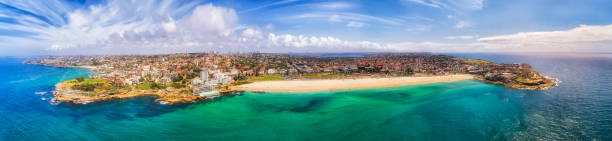 D Bondi Front wide day pan Wanderful Bondi blue colour of warm smooth water on white sands of Bondi beach of Sydney in wide aerial panorama. bondi junction stock pictures, royalty-free photos & images