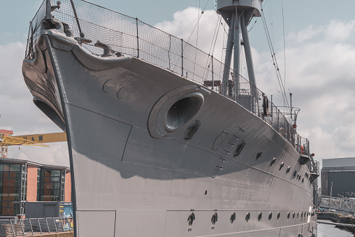 Belfast, Northern Ireland, United Kingdom - June 13, 2020:  The hull of HMS Caroline, a decommissioned C Class light cruiser built in 1914 and which was engaged the Battle of Jutland.  In the distance are the yellow cranes of Harland and Wolff's shipyard.