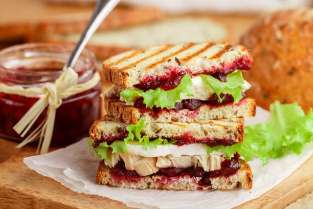 délicieux sandwich à la dinde ou au poulet au brie ou au camembert, laitue et canneberge (lingonberry, cowberry) chutney sur pain de céréales avec graines de lin. petit déjeuner gastronomique. panini. mise au point sélective - sandwich turkey cranberry cheese photos et images de collection