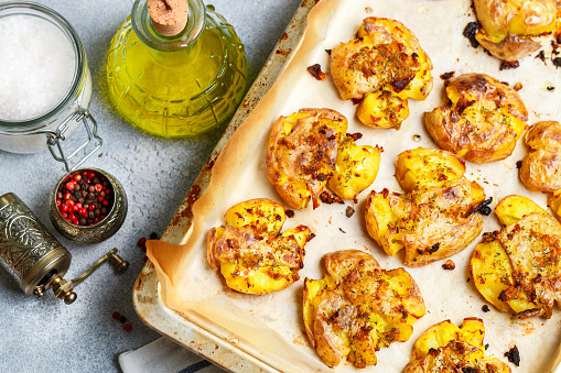 Oven baked whole crushed and crusty potato with coarse sea salt, olive oil, garlic, pepper and thyme in metallic tray. Roasted smashed potatoes. Australian cuisine dish. Selective focus