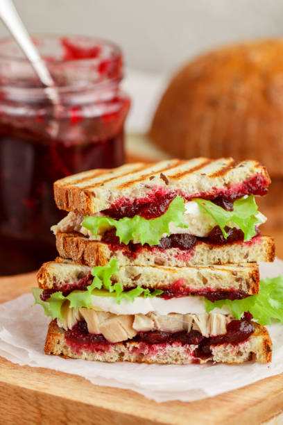 delicioso peru ou sanduíche de frango com brie ou queijo camembert, alface e cranberry (lingonberry, cowberry) chutney no pão de grãos com semente de linho. café da manhã gourmet. panini. foco seletivo - sandwich turkey cranberry cheese - fotografias e filmes do acervo