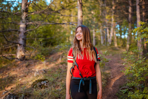 Pretty young woman hiking in the woods. She is wearing a red t-shirt. She is smiling.