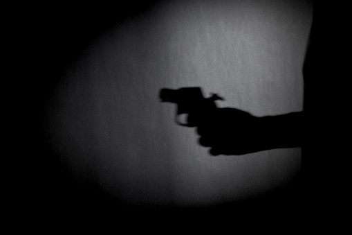 man with gun silhouette over dark wall. black and white photo can be used for illustrating horror and violence attack. crime concept. simple. selective focus. blurred.
