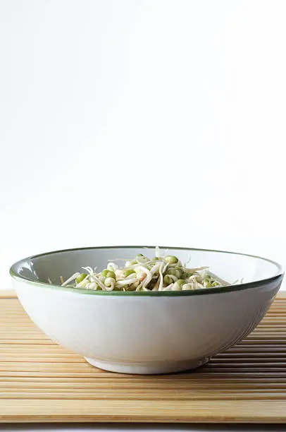 A bowl of mung beansprouts on a bamboo placemat with copy space above.  Portrait (vertiical) orientation.