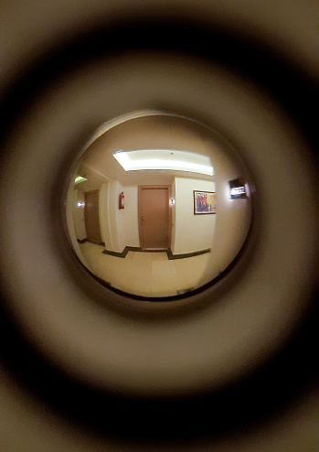 A corridor, burning lamps, a floor and two neighboring doors are visible in the door peephole