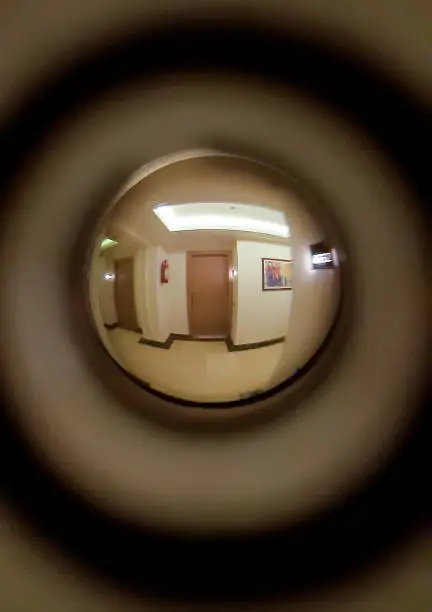 A corridor, burning lamps, a floor and two neighboring doors are visible in the door peephole