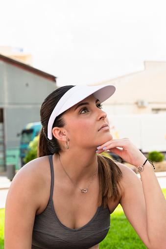 Close up of a young beautiful woman with sport visor and sport bra with her hand under her chin on an out of focus background. Healthy lifestyle and sport concept.