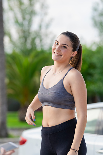 Beautiful young woman wearing a sport bra and tights smiling and looking at the camera on an out of focus background. Healthy lifestyle and sport concept.